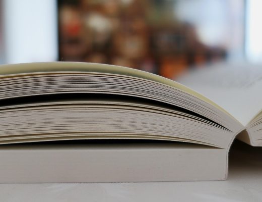 动漫共和国资料编辑在图书馆式的资料室里翻阅制作年表，手指停在目录页上核对年份，暖色书架背景延伸至画面深处